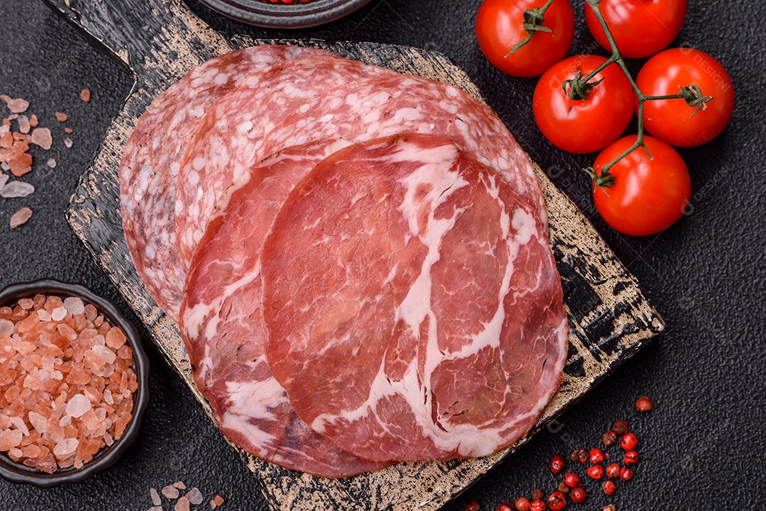 A imagem mostra um prato de embutidos, com destaque para fatias de salame e presunto cru, acompanhados de tomates-cereja e pimenta rosa