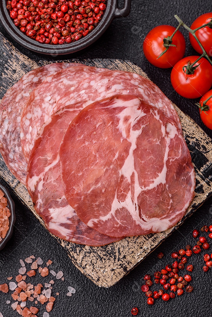 A imagem mostra um prato de embutidos, com destaque para fatias de salame e presunto cru, acompanhados de tomates-cereja e pimenta rosa
