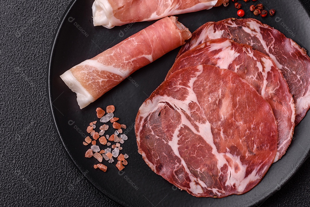 A imagem mostra um prato de embutidos, com destaque para fatias de salame e presunto cru, acompanhados de tomates-cereja e pimenta rosa