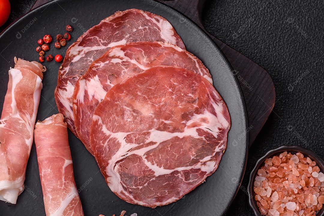 A imagem mostra um prato de embutidos, com destaque para fatias de salame e presunto cru, acompanhados de tomates-cereja e pimenta rosa