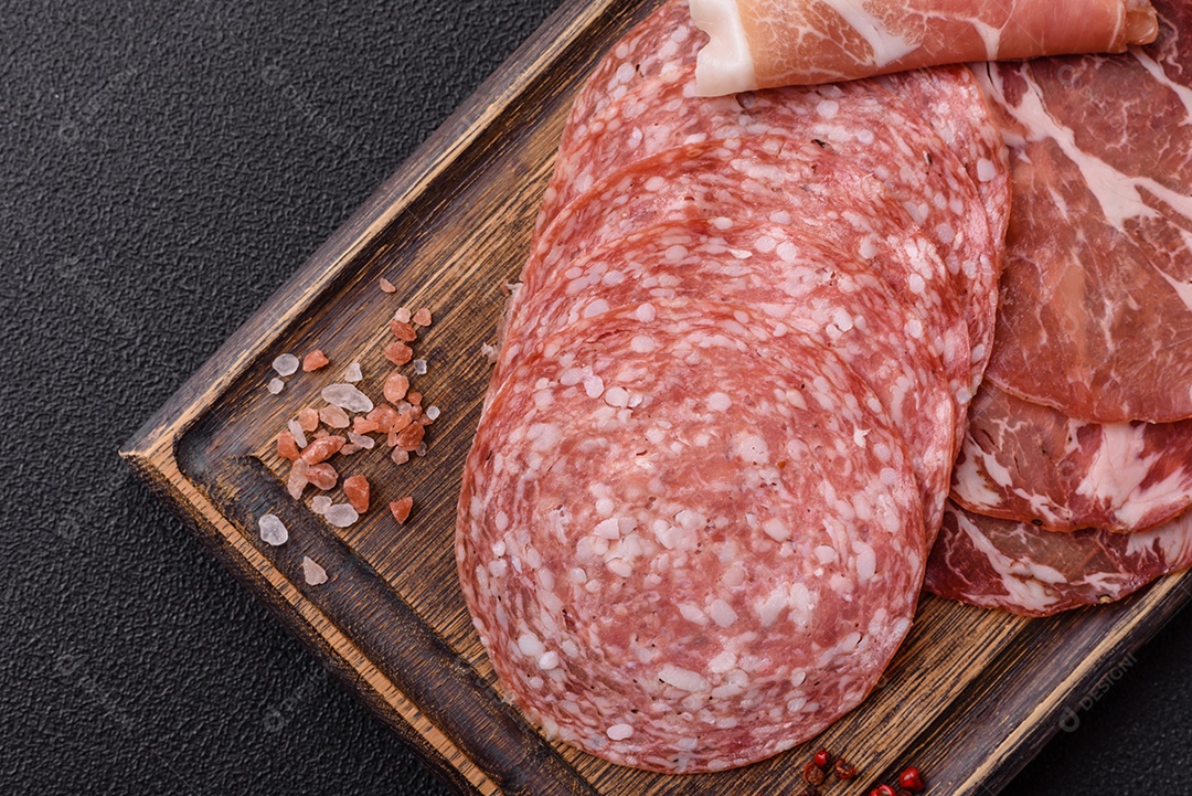 A imagem mostra um prato de embutidos, com destaque para fatias de salame e presunto cru, acompanhados de tomates-cereja e pimenta rosa