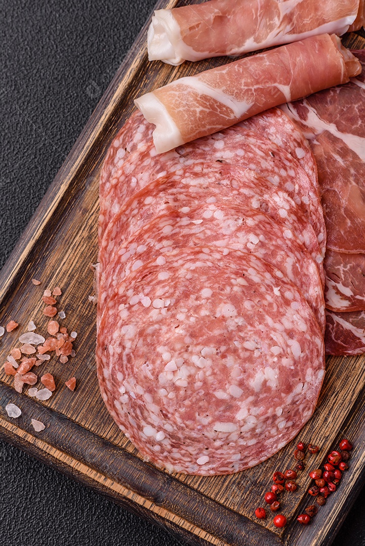 A imagem mostra um prato de embutidos, com destaque para fatias de salame e presunto cru, acompanhados de tomates-cereja e pimenta rosa