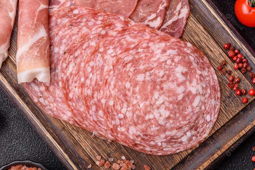 A imagem mostra um prato de embutidos, com destaque para fatias de salame e presunto cru, acompanhados de tomates-cereja e pimenta rosa