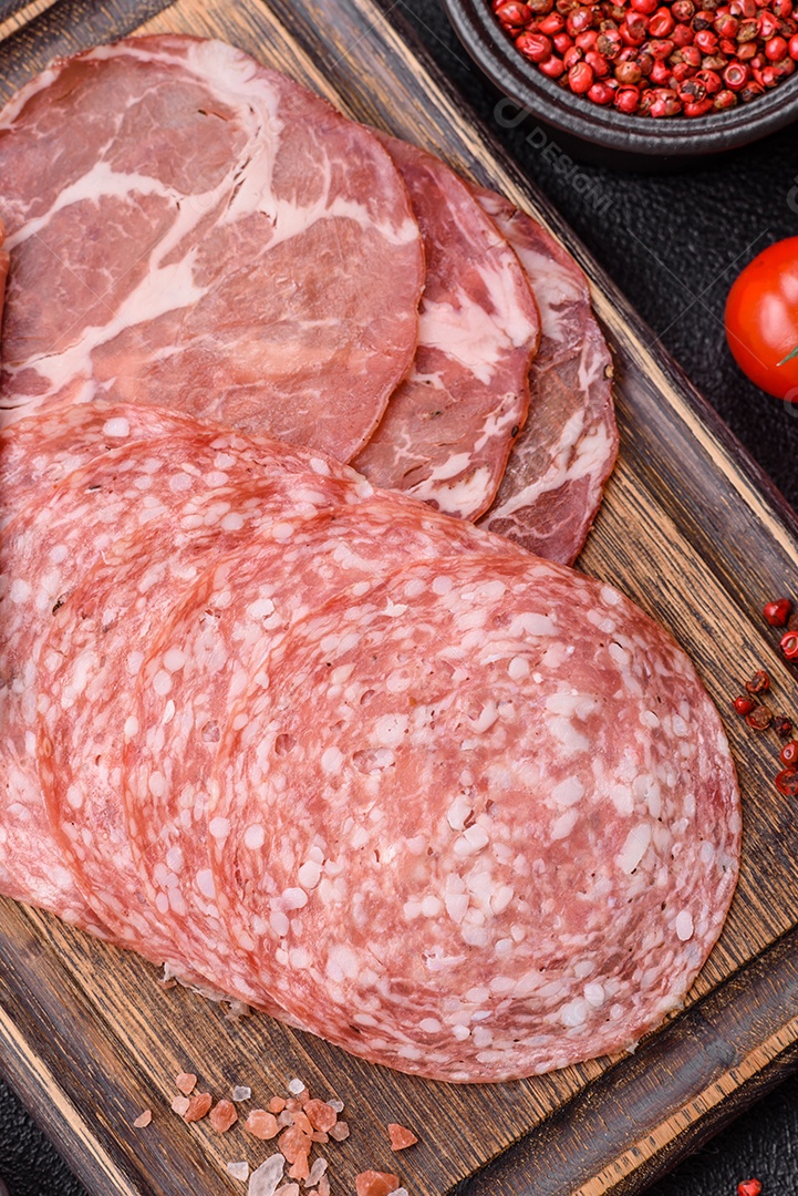 A imagem mostra um prato de embutidos, com destaque para fatias de salame e presunto cru, acompanhados de tomates-cereja e pimenta rosa