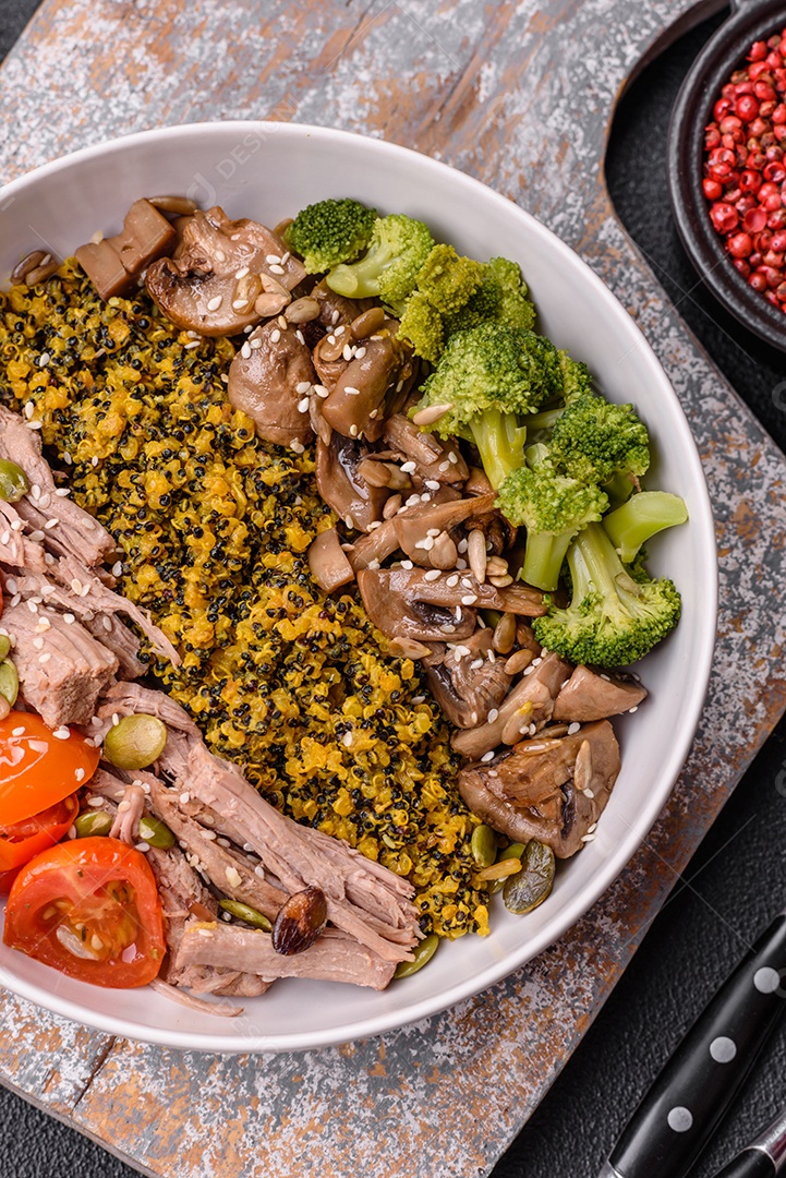 A imagem mostra uma tigela de quinoa com brócolis, cogumelos, carne desfiada (possivelmente frango ou carne bovina), tomate cereja e sementes de abóbora