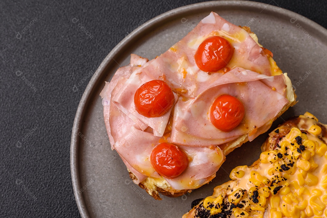 A imagem mostra um sanduíche de brioche com presunto, queijo derretido e tomates cereja, polvilhado com sal e pimenta.