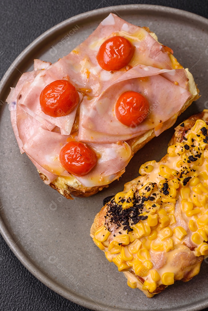 A imagem mostra um sanduíche de brioche com presunto, queijo derretido e tomates cereja, polvilhado com sal e pimenta.