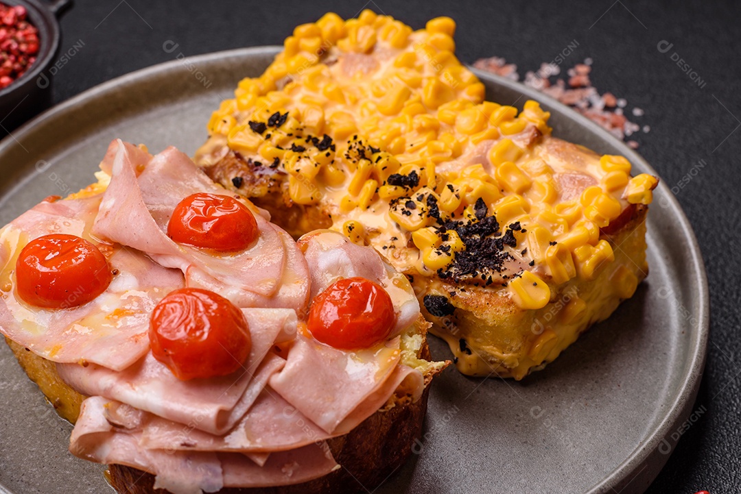 A imagem mostra um sanduíche de brioche com presunto, queijo derretido e tomates cereja, polvilhado com sal e pimenta.