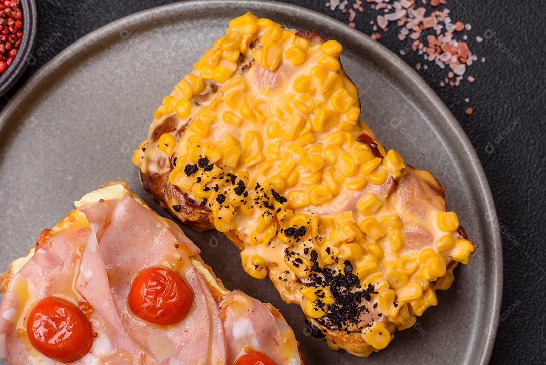 A imagem mostra um sanduíche de brioche com presunto, queijo derretido e tomates cereja, polvilhado com sal e pimenta.