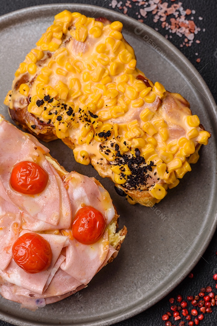 A imagem mostra um sanduíche de brioche com presunto, queijo derretido e tomates cereja, polvilhado com sal e pimenta.
