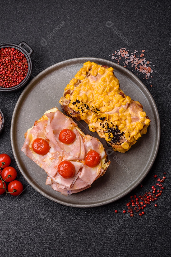 A imagem mostra um sanduíche de brioche com presunto, queijo derretido e tomates cereja, polvilhado com sal e pimenta.