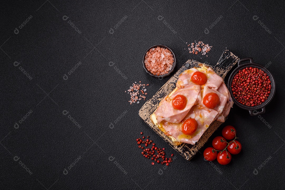 A imagem mostra um sanduíche de brioche com presunto, queijo derretido e tomates cereja, polvilhado com sal e pimenta.