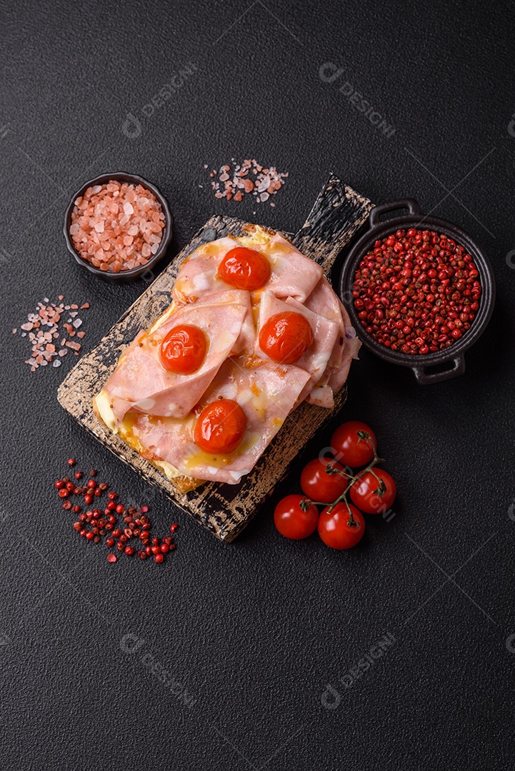 A imagem mostra um sanduíche de brioche com presunto, queijo derretido e tomates cereja, polvilhado com sal e pimenta.