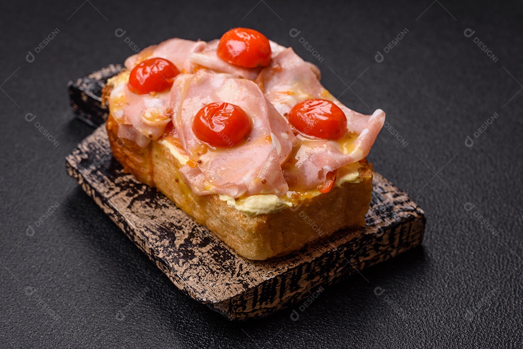 A imagem mostra um sanduíche de brioche com presunto, queijo derretido e tomates cereja, polvilhado com sal e pimenta.