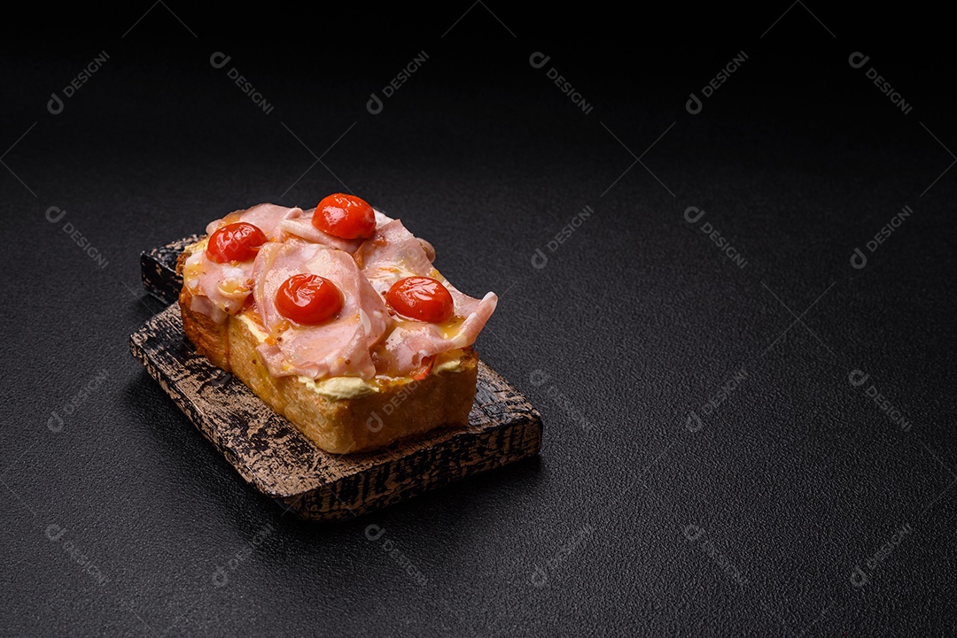 A imagem mostra um sanduíche de brioche com presunto, queijo derretido e tomates cereja, polvilhado com sal e pimenta.