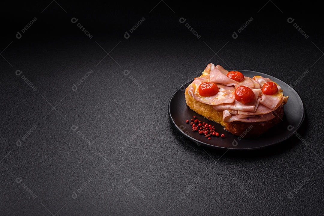 A imagem mostra um sanduíche de brioche com presunto, queijo derretido e tomates cereja, polvilhado com sal e pimenta.