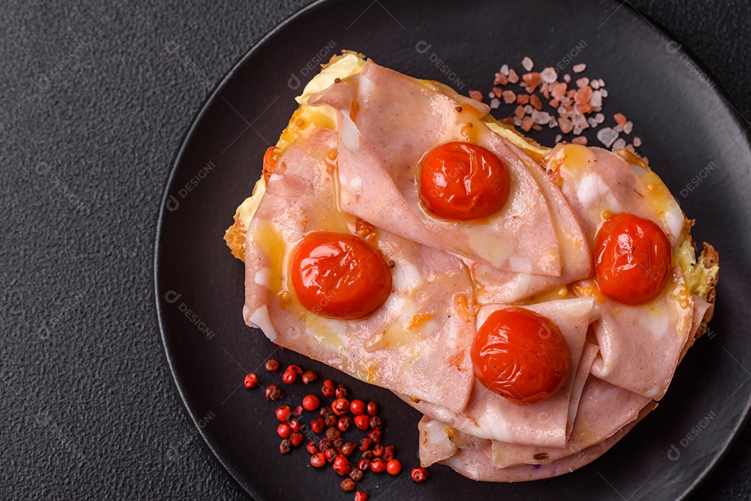 A imagem mostra um sanduíche de brioche com presunto, queijo derretido e tomates cereja, polvilhado com sal e pimenta.