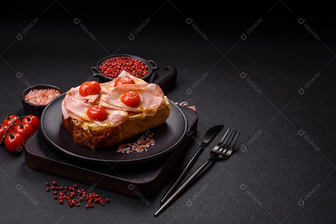 A imagem mostra um sanduíche de brioche com presunto, queijo derretido e tomates cereja, polvilhado com sal e pimenta.