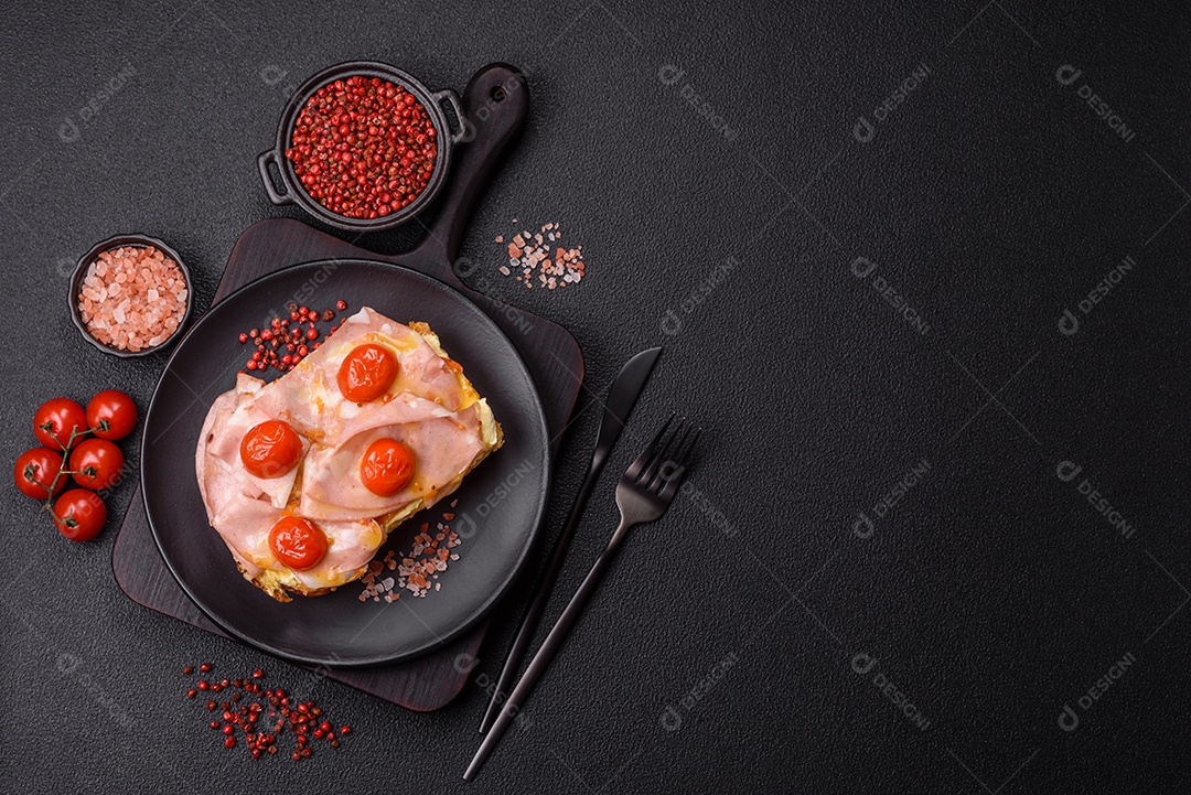A imagem mostra um sanduíche de brioche com presunto, queijo derretido e tomates cereja, polvilhado com sal e pimenta.