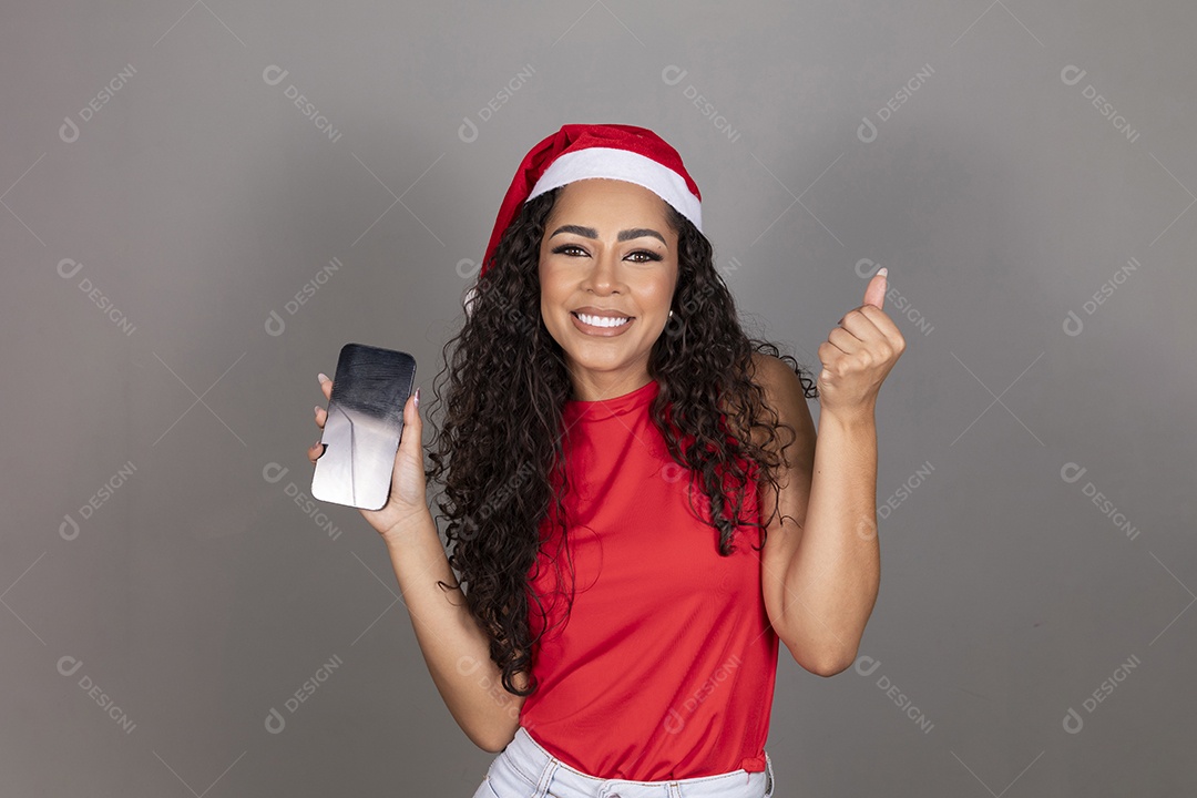 Linda jovem morena cabelo cacheado usando gorro do papai noel segurando celular smartphone