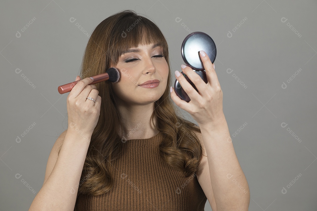 Linda mulher jovem se maquiando sobre fundo isolado branco