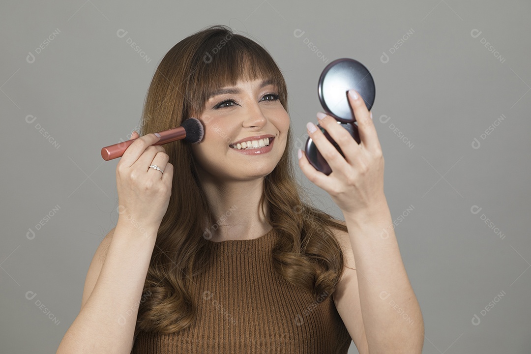 Linda mulher jovem se maquiando sobre fundo isolado branco