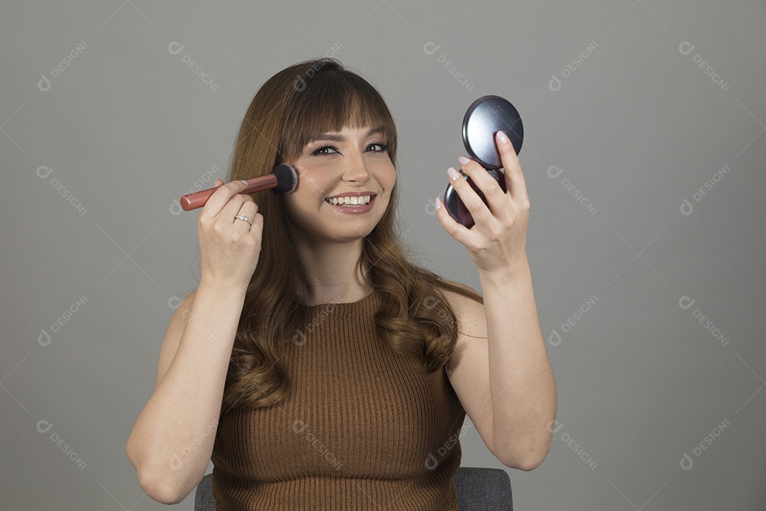 Linda mulher jovem se maquiando sobre fundo isolado branco