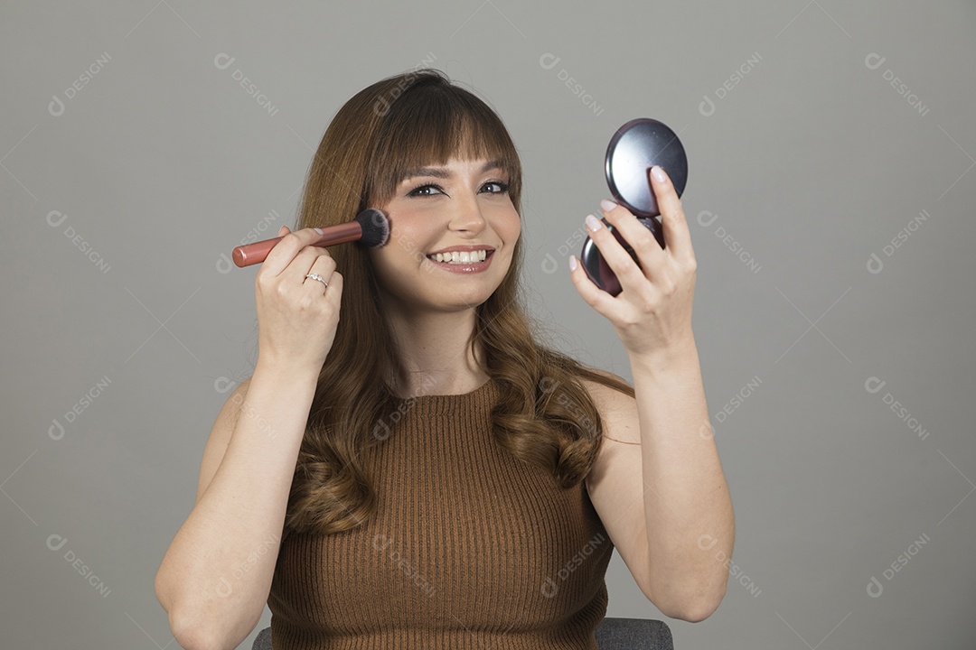 Linda mulher jovem se maquiando sobre fundo isolado branco