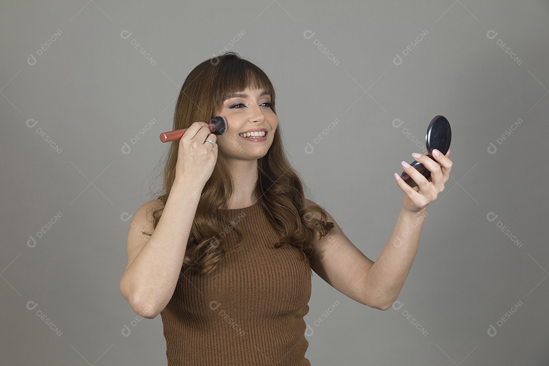 Linda mulher jovem se maquiando sobre fundo isolado branco