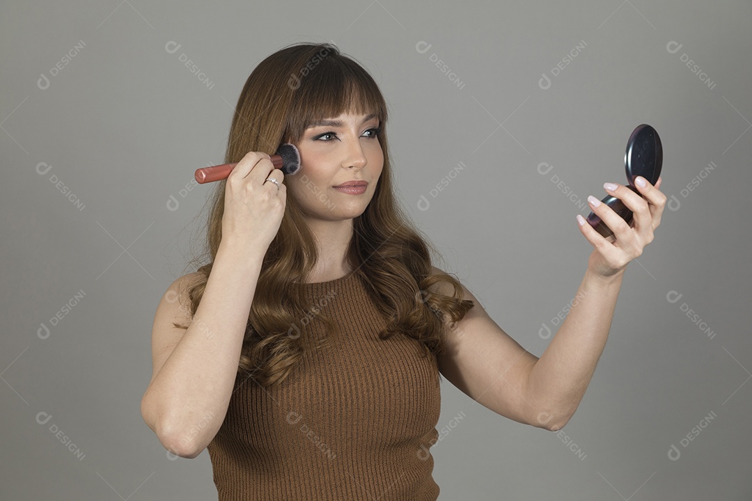 Linda mulher jovem se maquiando sobre fundo isolado branco