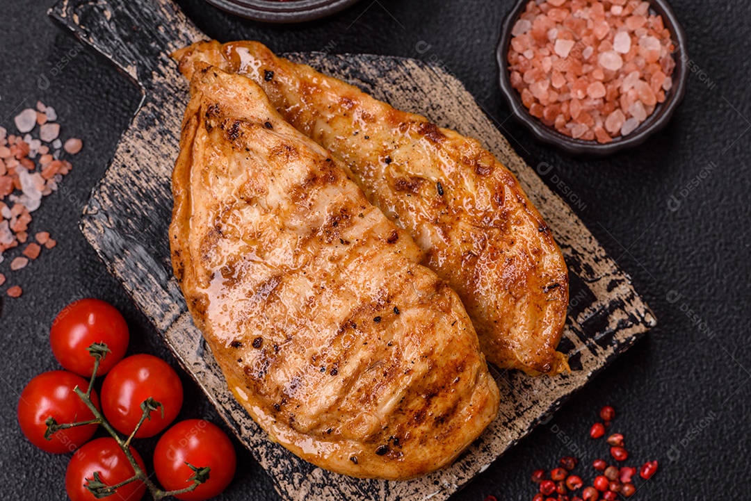 A imagem mostra filés de frango grelhados, acompanhados de temperos e tomates cereja.