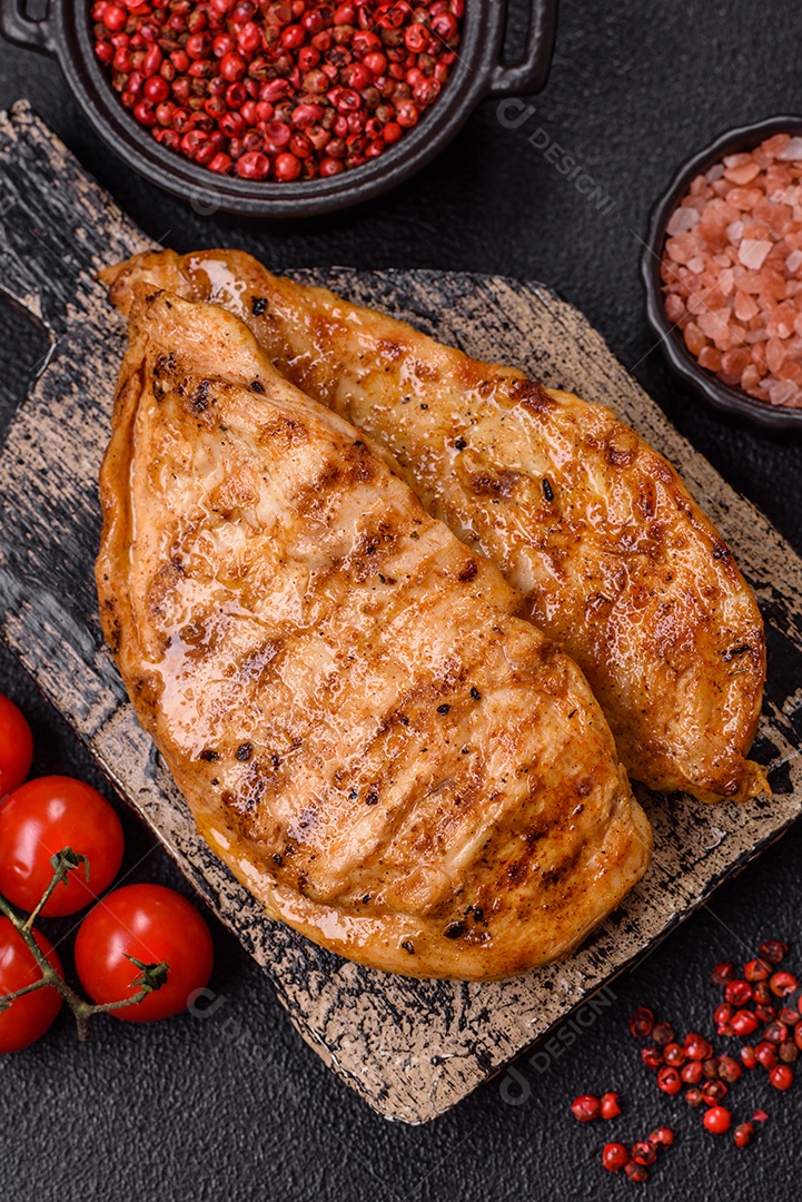 A imagem mostra filés de frango grelhados, acompanhados de temperos e tomates cereja.