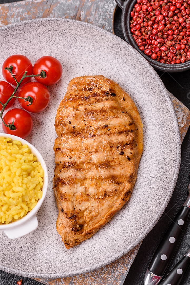 A imagem mostra filés de frango grelhados, acompanhados de temperos e tomates cereja.