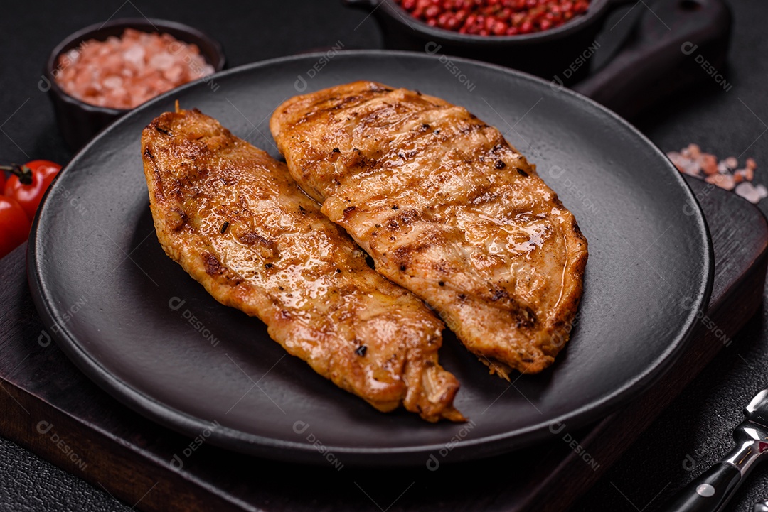 A imagem mostra filés de frango grelhados, acompanhados de temperos e tomates cereja.