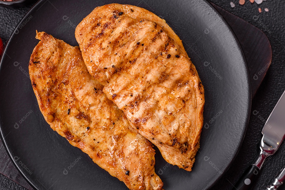 A imagem mostra filés de frango grelhados, acompanhados de temperos e tomates cereja.