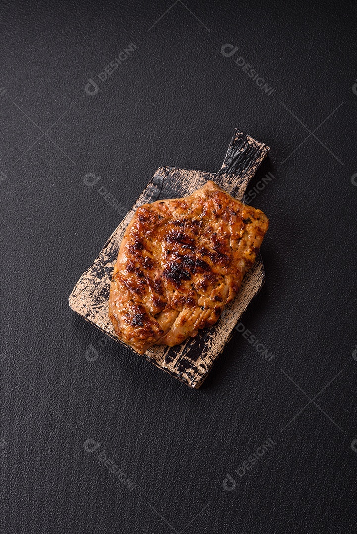 A imagem mostra um pedaço de carne grelhada ou assada, possivelmente frango ou porco, servido em uma tábua de madeira