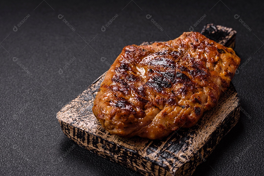 A imagem mostra um pedaço de carne grelhada ou assada, possivelmente frango ou porco, servido em uma tábua de madeira