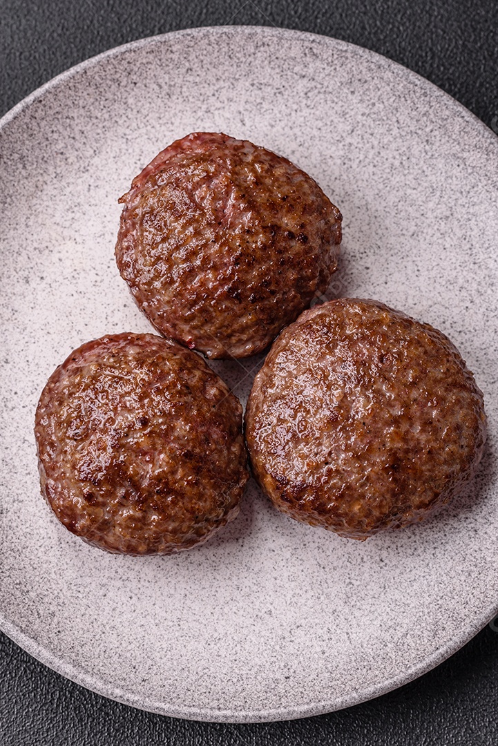 A imagem mostra dois hambúrgueres (ou bifes de carne moída) em um prato preto, acompanhados por tomates cereja