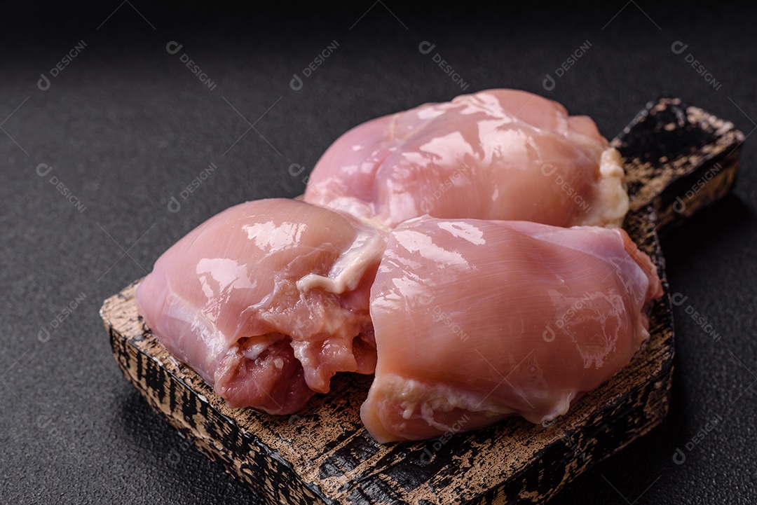 A imagem mostra dois filés de peito de frango crus sobre uma tábua de madeira