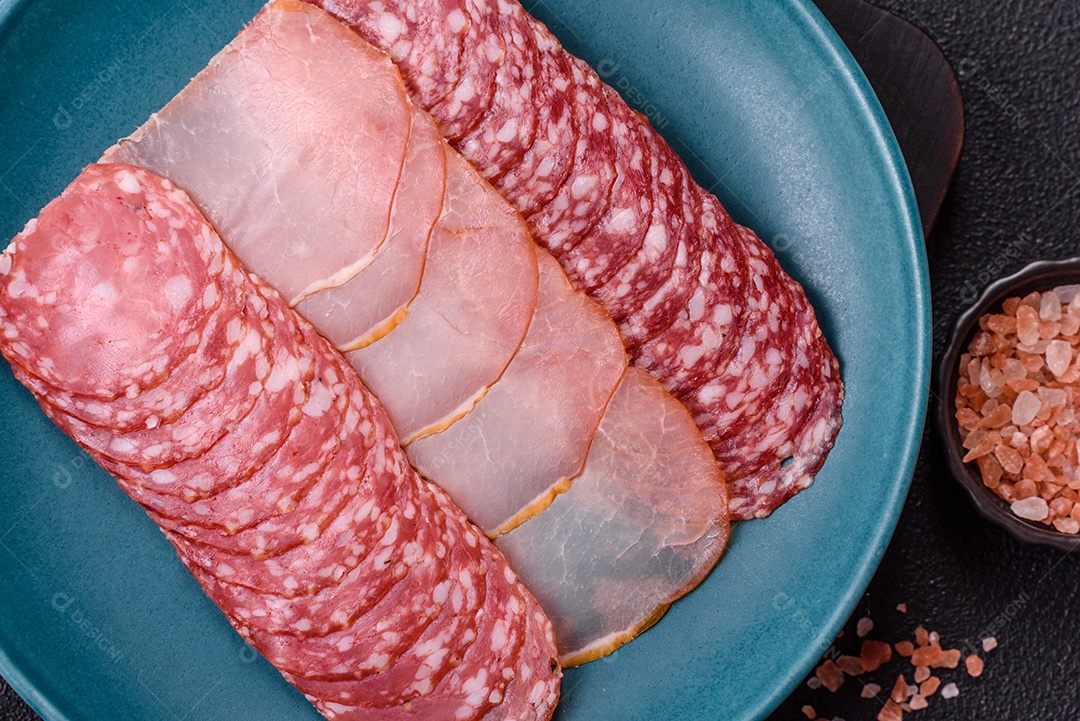 A imagem mostra uma tábua com fatias de salame e presunto, acompanhadas de temperos e especiarias como pimenta-do-reino e páprica.
