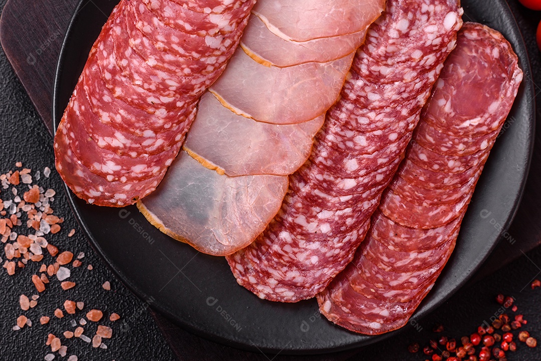 A imagem mostra uma tábua com fatias de salame e presunto, acompanhadas de temperos e especiarias como pimenta-do-reino e páprica.