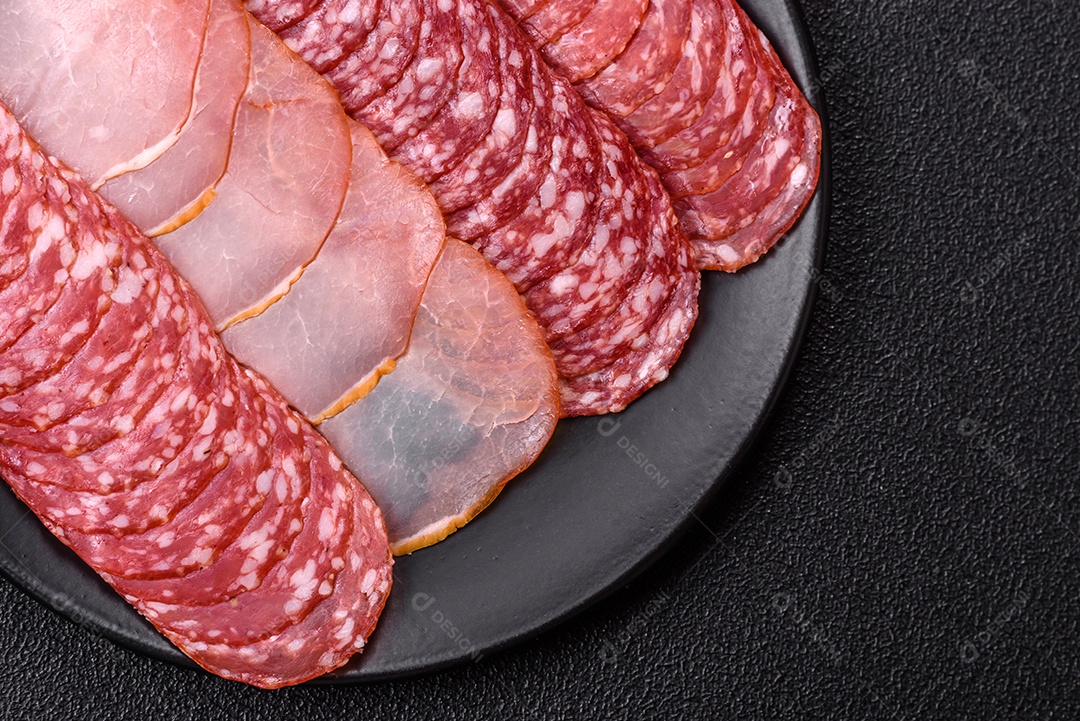 A imagem mostra uma tábua com fatias de salame e presunto, acompanhadas de temperos e especiarias como pimenta-do-reino e páprica.