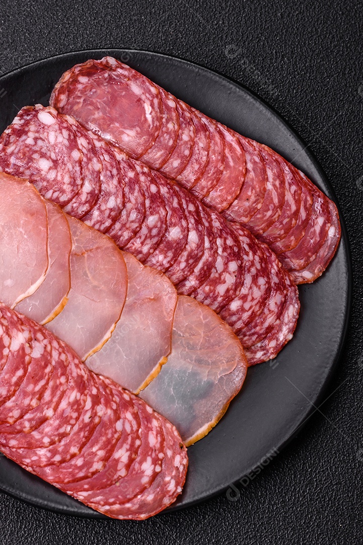 A imagem mostra uma tábua com fatias de salame e presunto, acompanhadas de temperos e especiarias como pimenta-do-reino e páprica.