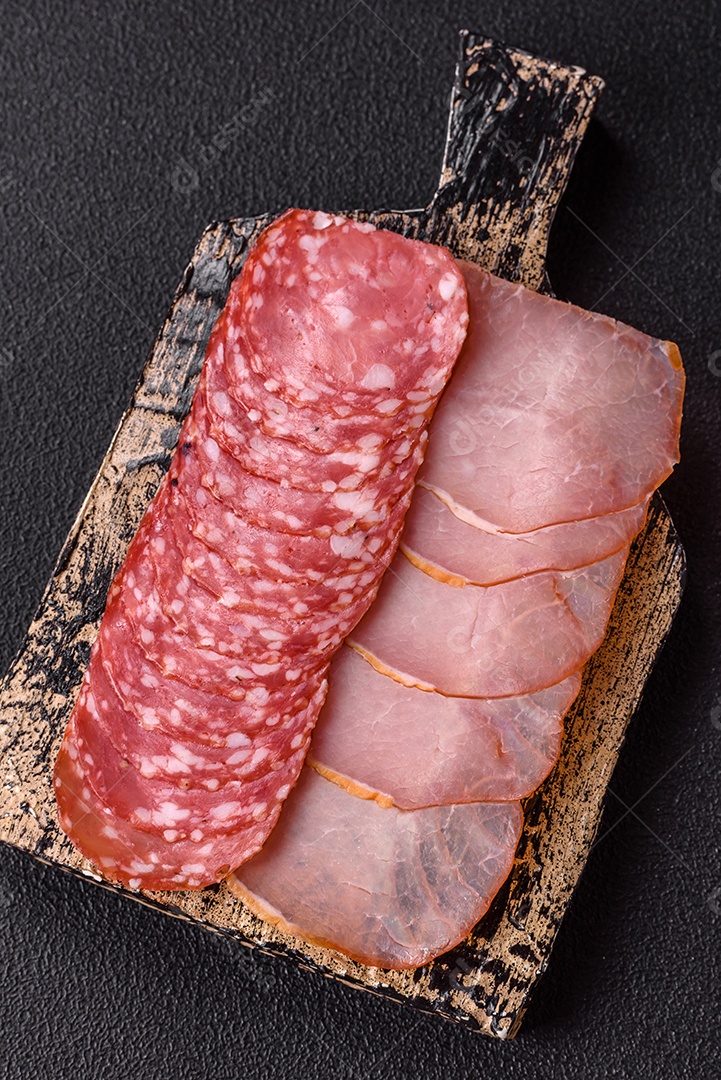 A imagem mostra uma tábua com fatias de salame e presunto, acompanhadas de temperos e especiarias como pimenta-do-reino e páprica.