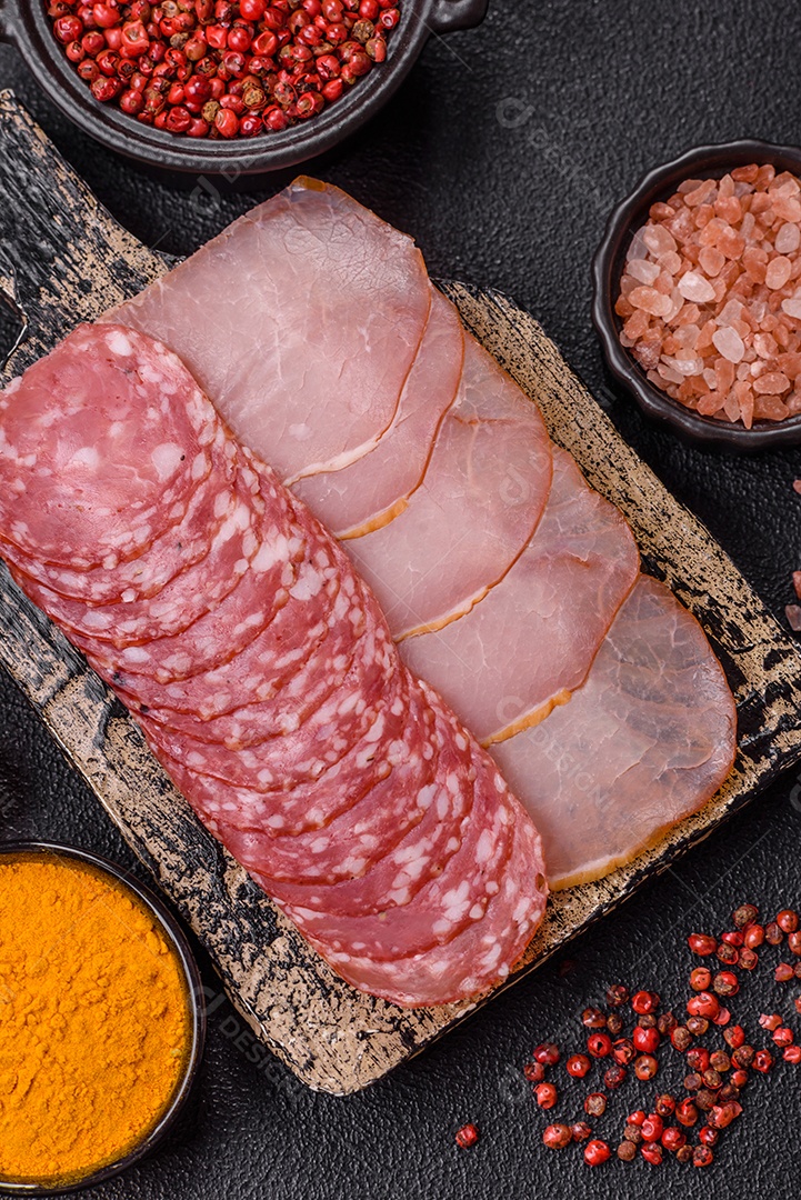 A imagem mostra uma tábua com fatias de salame e presunto, acompanhadas de temperos e especiarias como pimenta-do-reino e páprica.