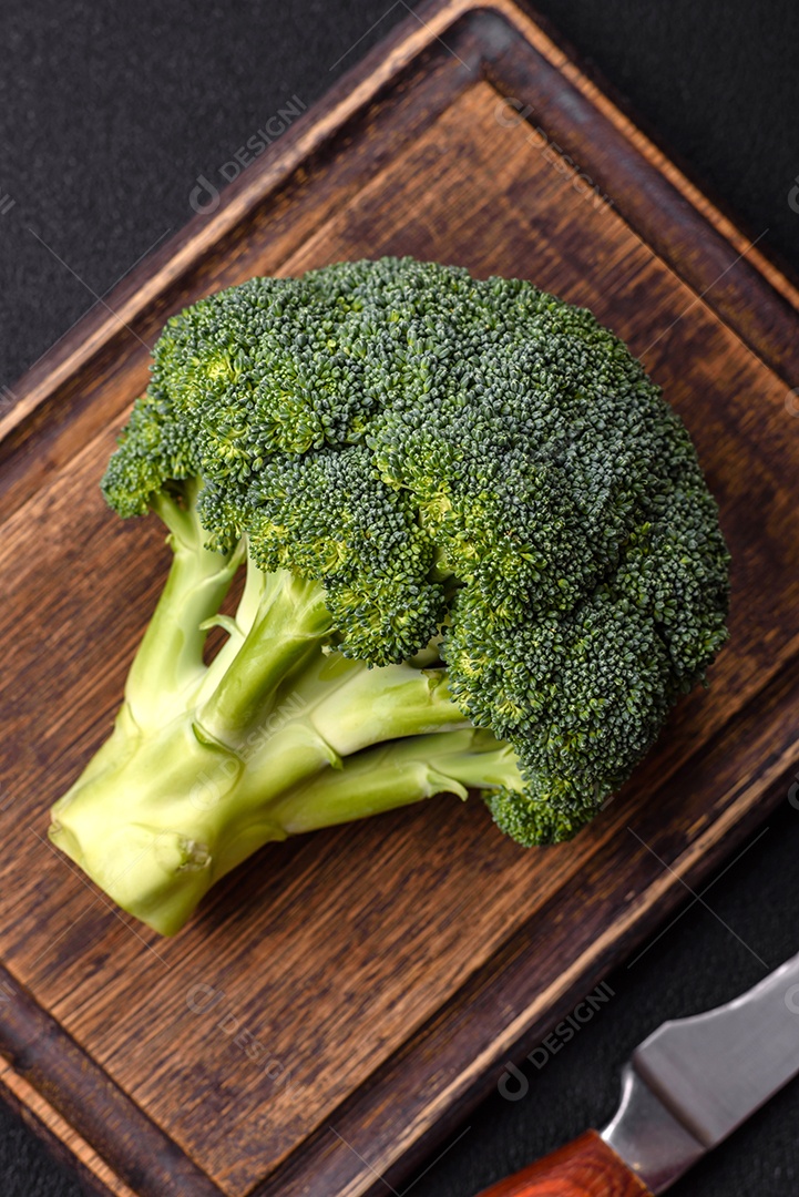 A imagem mostra um brócolis em uma tábua de corte de madeira.