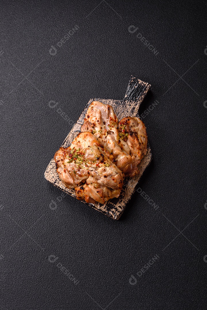 A imagem mostra sobrecoxas de frango grelhadas, servidas em um prato escuro com temperos