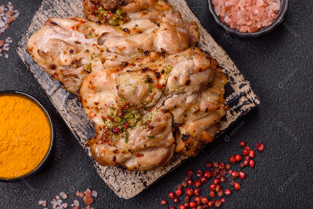 A imagem mostra sobrecoxas de frango grelhadas, servidas em um prato escuro com temperos