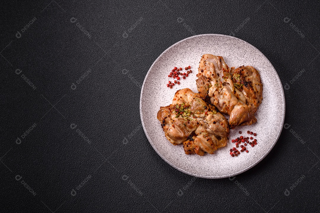 A imagem mostra sobrecoxas de frango grelhadas, servidas em um prato escuro com temperos