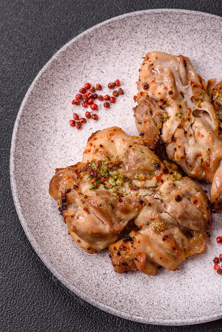 A imagem mostra sobrecoxas de frango grelhadas, servidas em um prato escuro com tempero